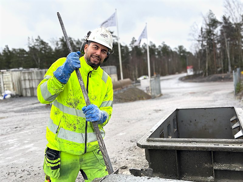 En man står utomhus i ett industriområdet och arbetar med betong