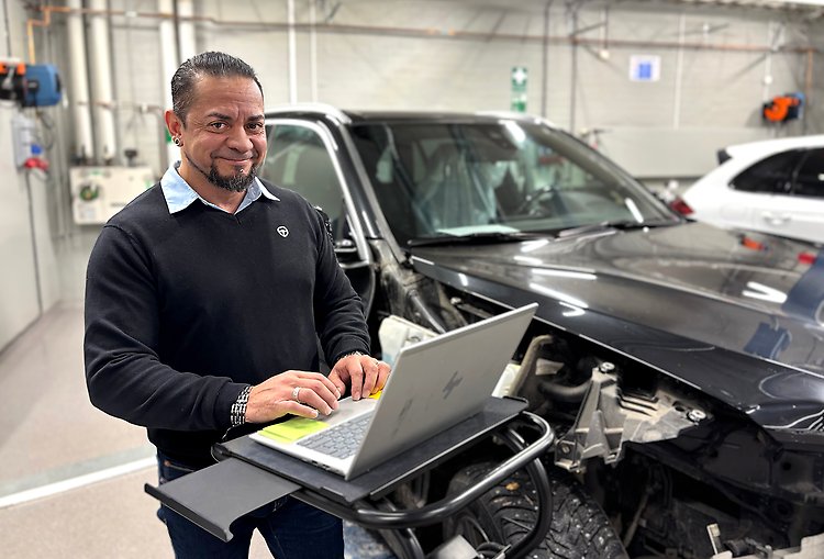 Man i skjorta och tröja står med en dator i en bilverkstad.
