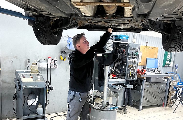Man som står under bil i bilverkstad